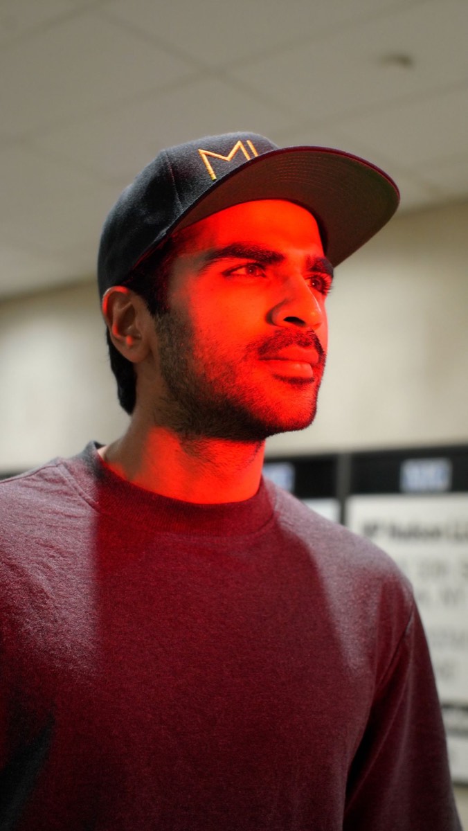 Portrait of Akhil Aryan, lit red, wearing a cap