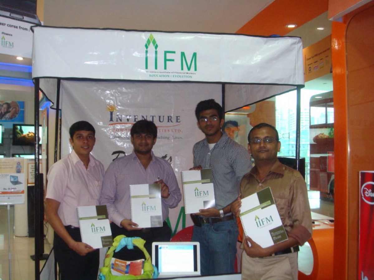Four of us behind a folding-table stall in a shopping mall, holding brochures